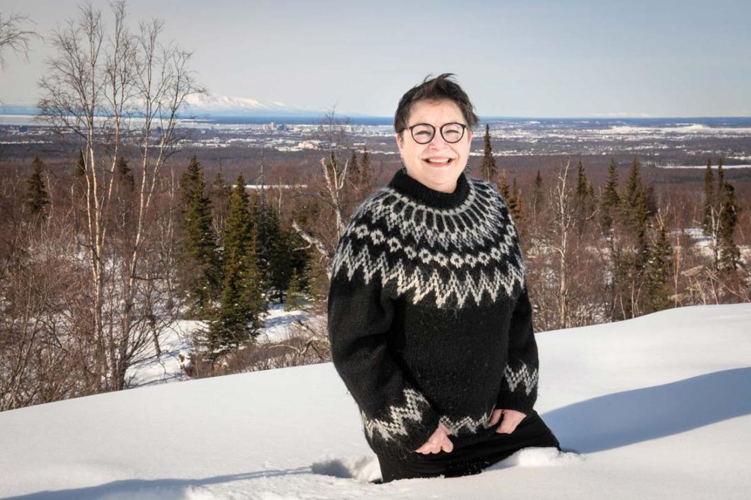 A woman in a Nordic sweater stands in the snow overlooking downtown Anchorage. 