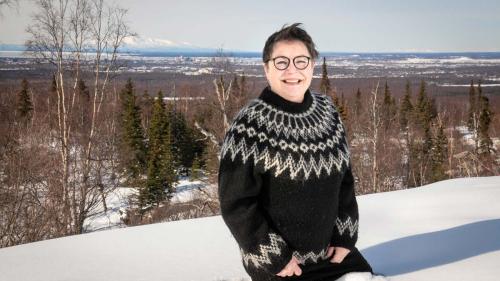 A woman in a Nordic sweater stands in the snow overlooking downtown Anchorage. 