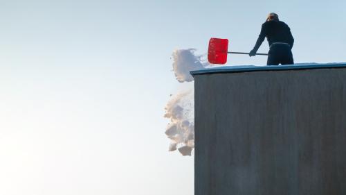 A person shovels snow on a roof